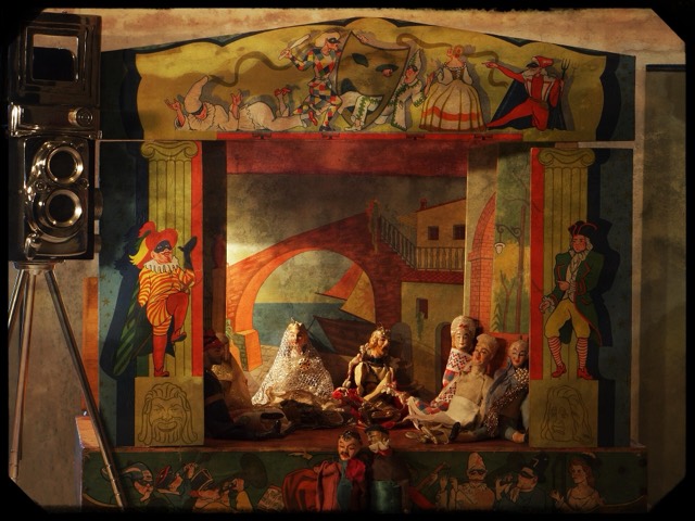 A small marionette theatre with painted scenery and puppets on stage, an old twin lens camera at one side