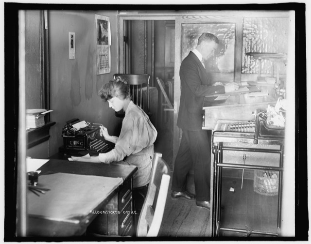 An accountant's office in the 1910s, a woman at a typewriter and a man working at a tall ledger desk