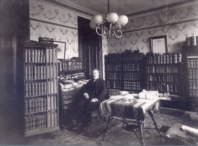A lawyer seated in his office in St. Louis, surrounded by glass-fronted cases of law books