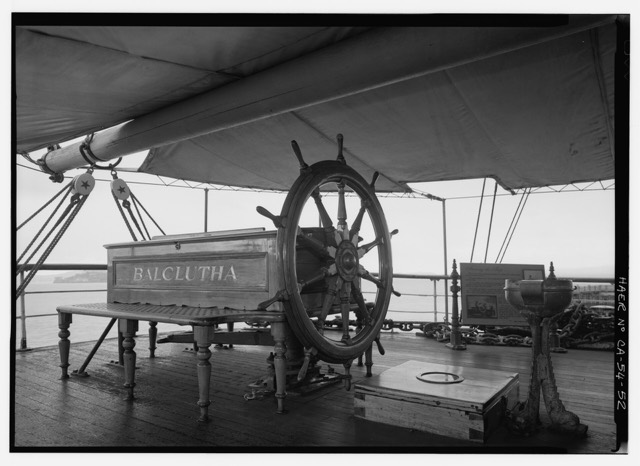 A ship's wheel and steering compass binnacle on the deck of a sailing ship