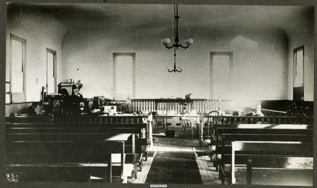 An empty courtroom in about 1885, with the judge's bench, railings and rows of benches