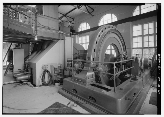 The inside of a hydroelectric powerhouse, with a large generator and an operator's platform