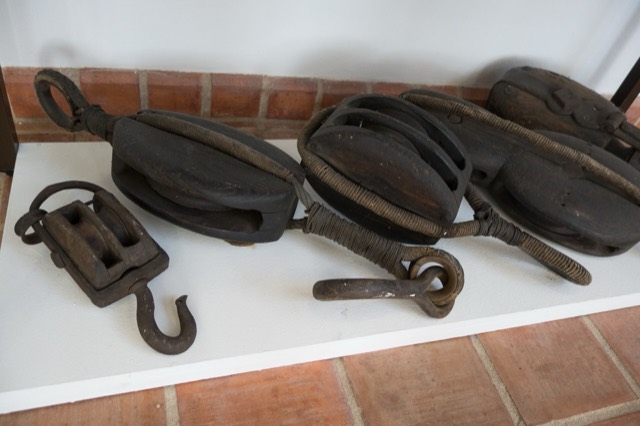 Old wooden pulley blocks with iron hooks, laid out on a shelf