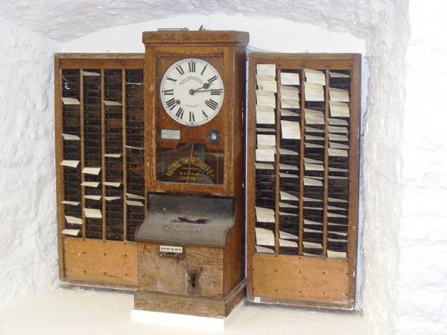 An old factory time clock between two racks of paper clocking-in cards