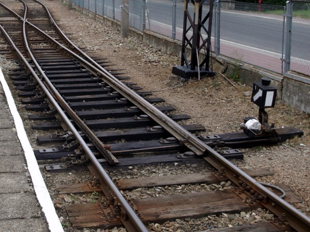 Railway tracks meeting at a manual points switch, with a lever beside the line