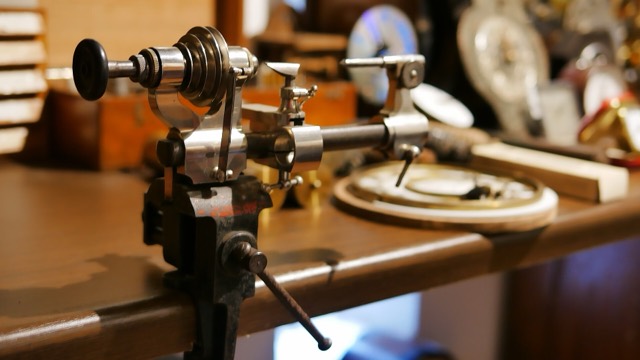 A close view of a small watchmaker's lathe clamped to a workbench