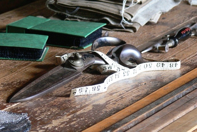 A tailor's shears, a tape measure and an iron on a worn wooden workbench